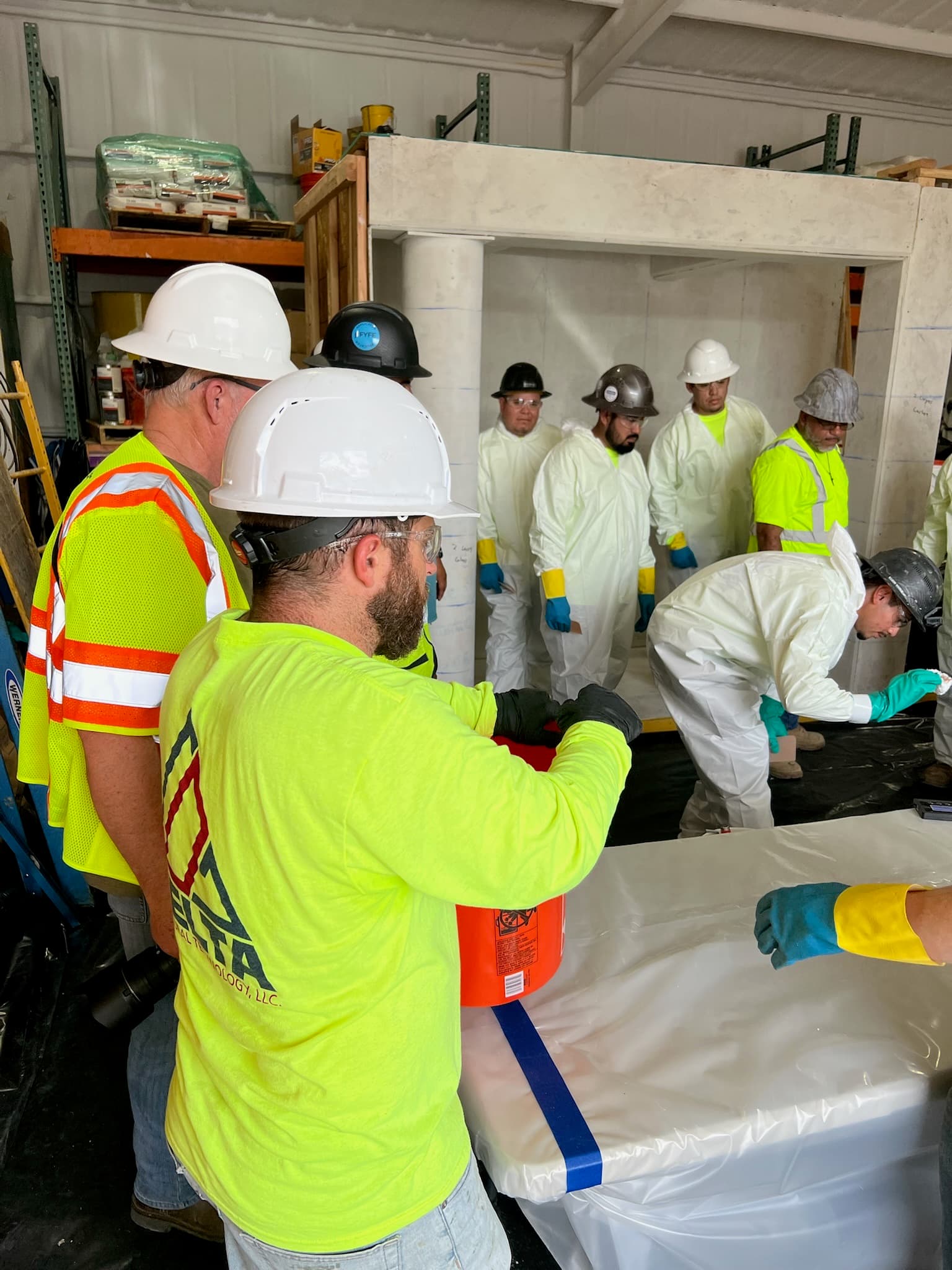 Delta instructor briefing trainees in protective suits at the training mock-up