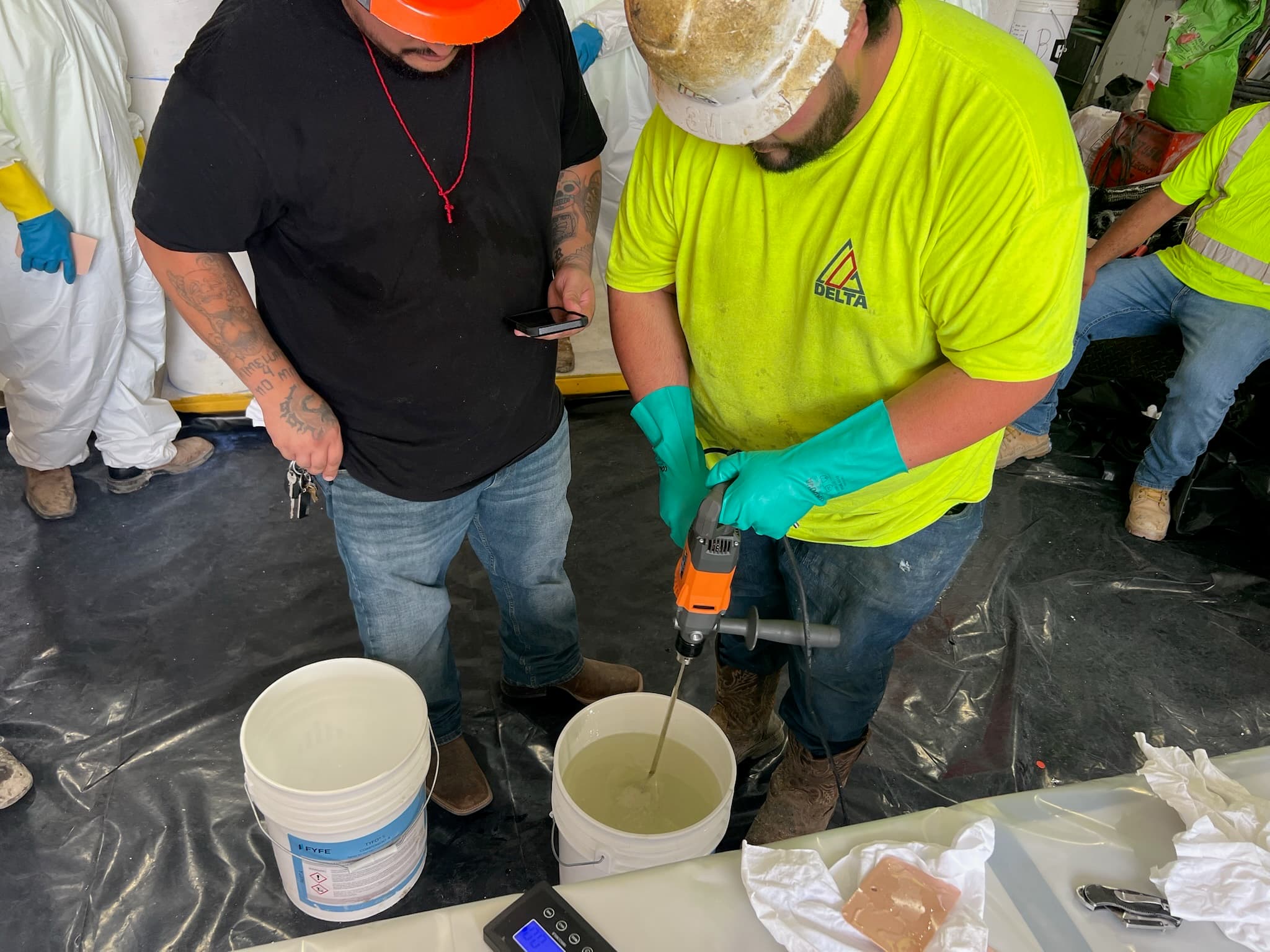 Trainee mixing epoxy resin with a paddle mixer while components are weighed