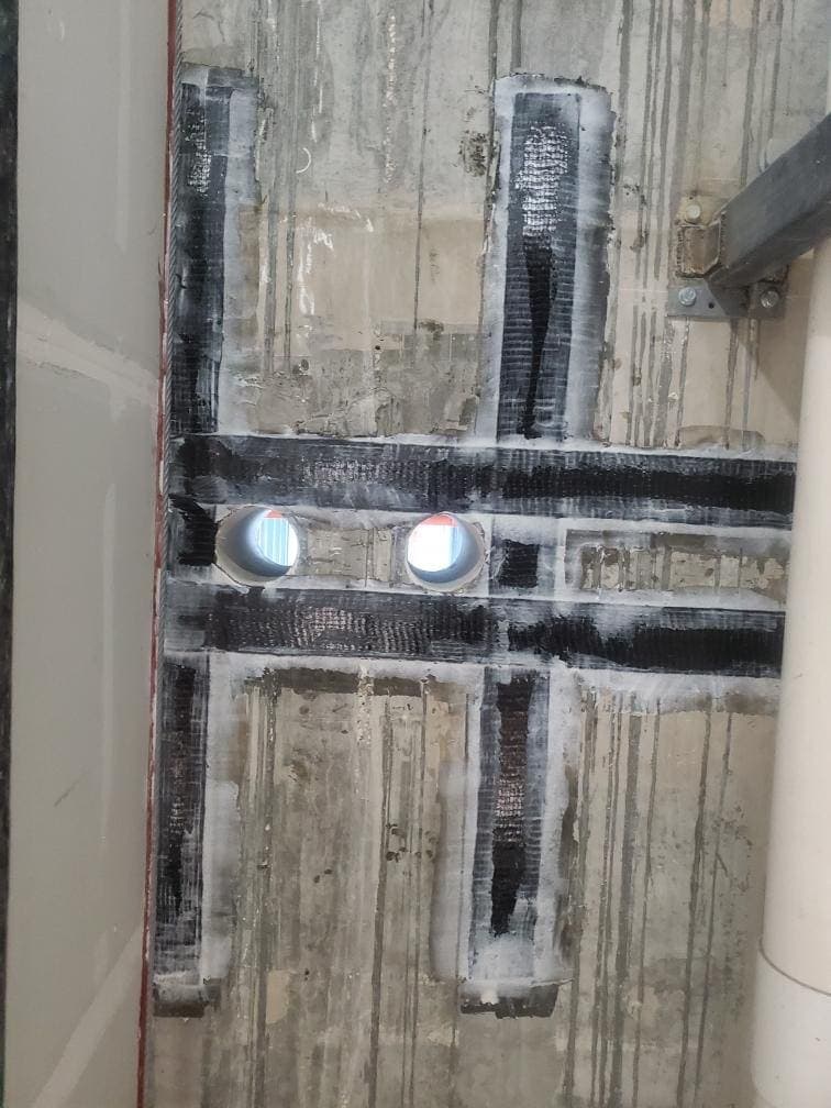 Black composite strips framing two pipe penetrations in a concrete wall.