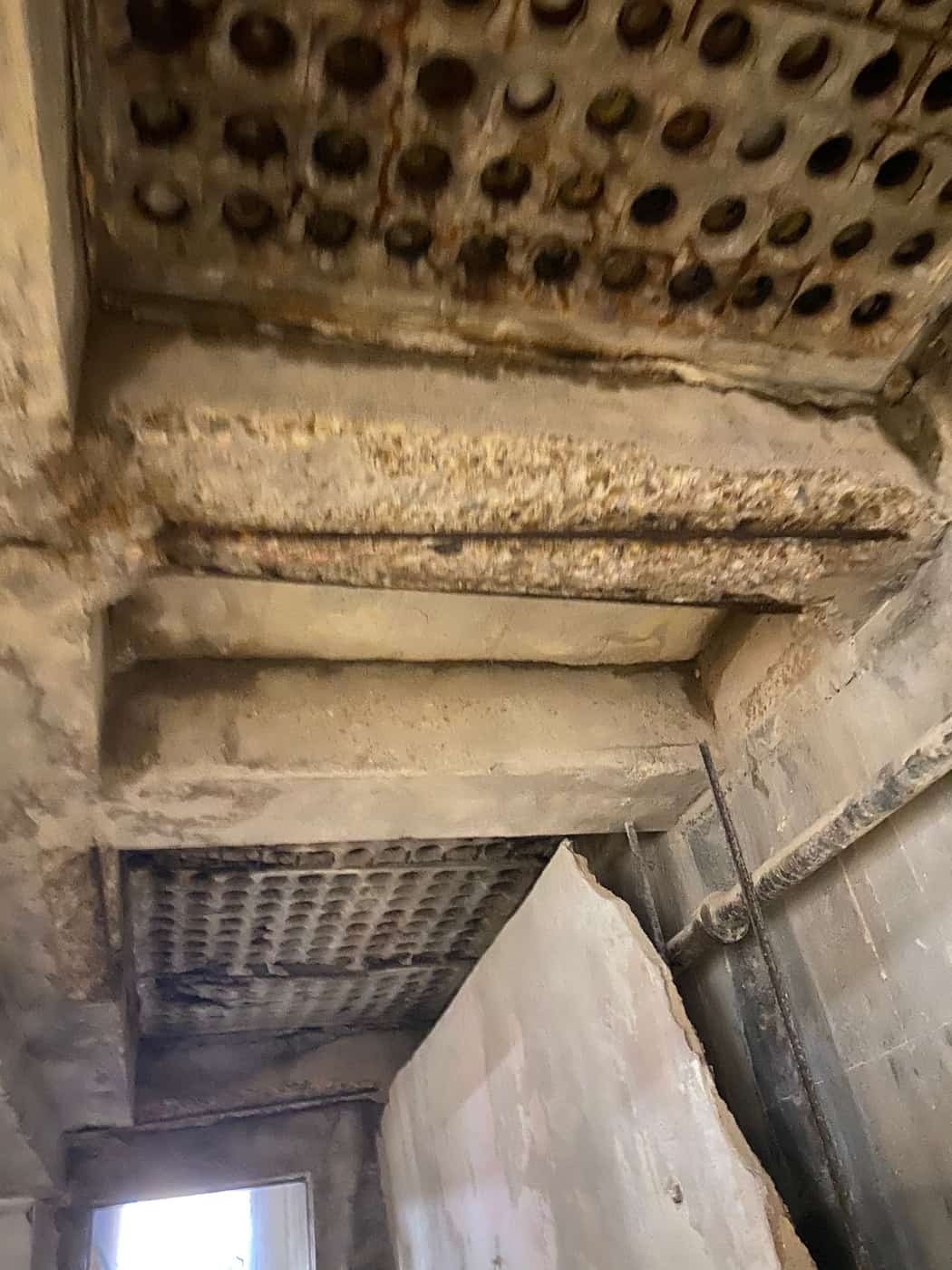 Slab underside with an exposed grid of round voids and a spalled beam.