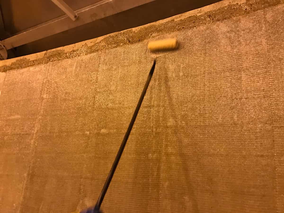 Roller on an extension pole saturating glass fiber fabric on a concrete tank wall.