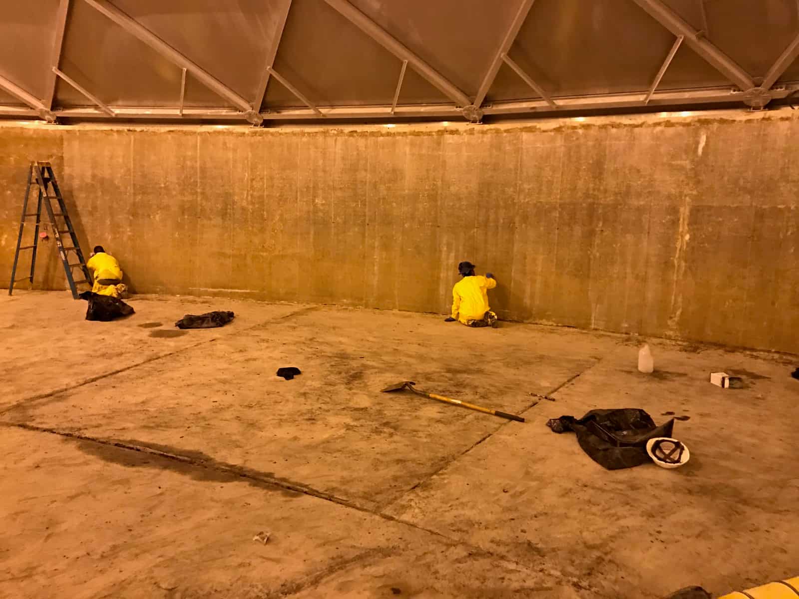 Inside a domed concrete tank with workers applying composite fabric to the interior wall.