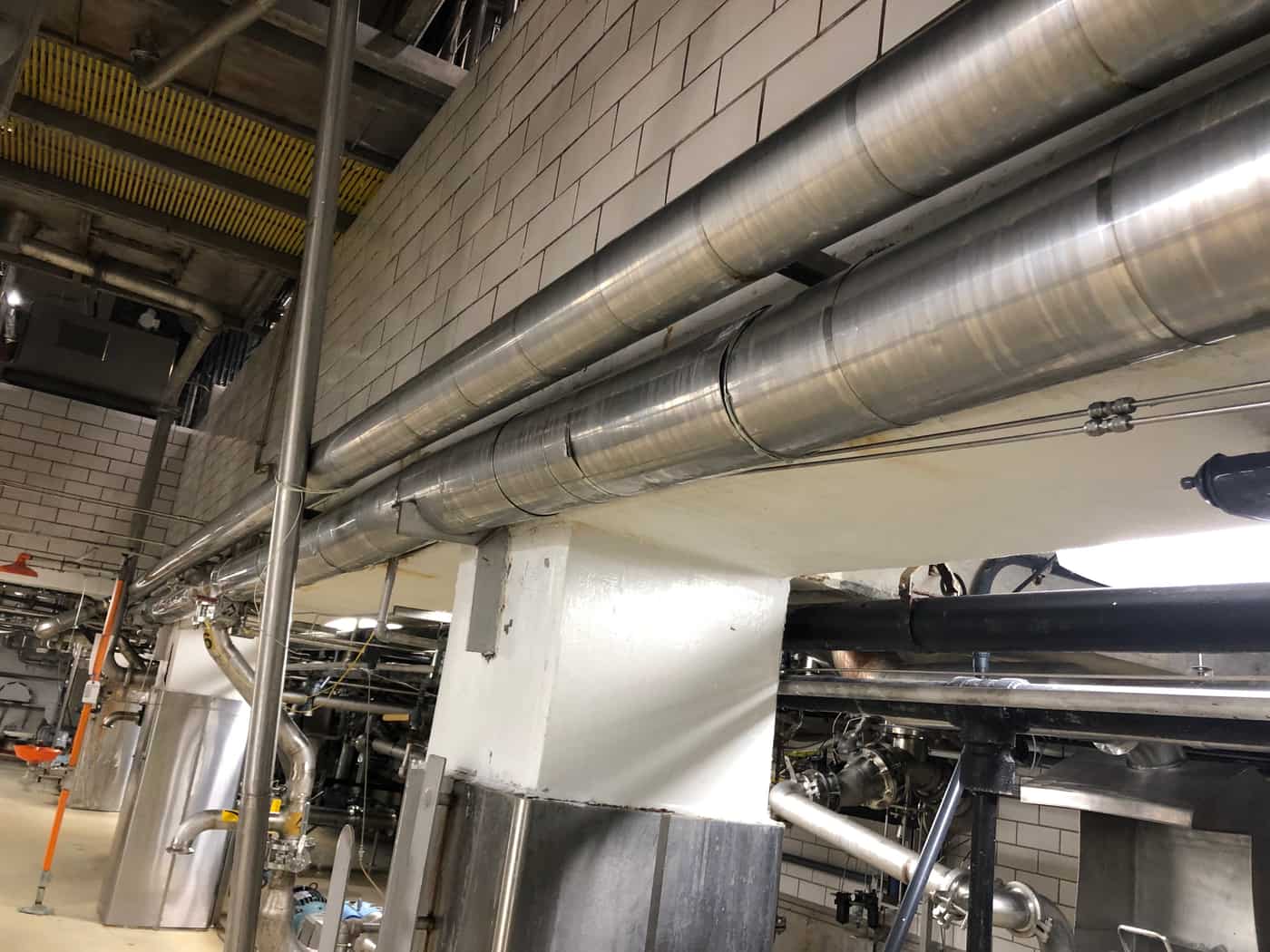 Concrete beam with insulated ducts and piping along a tiled production corridor.