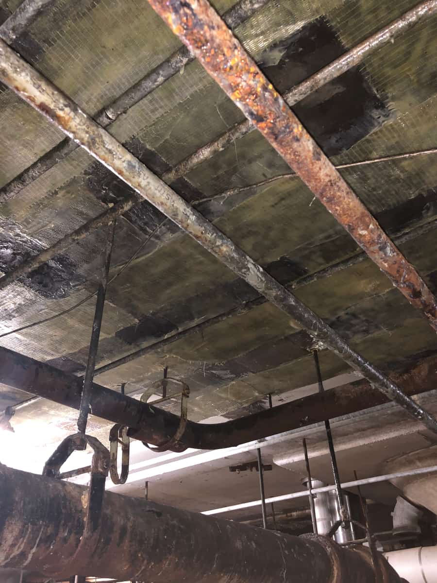 Wrapped slab underside with rusted pipe hangers.