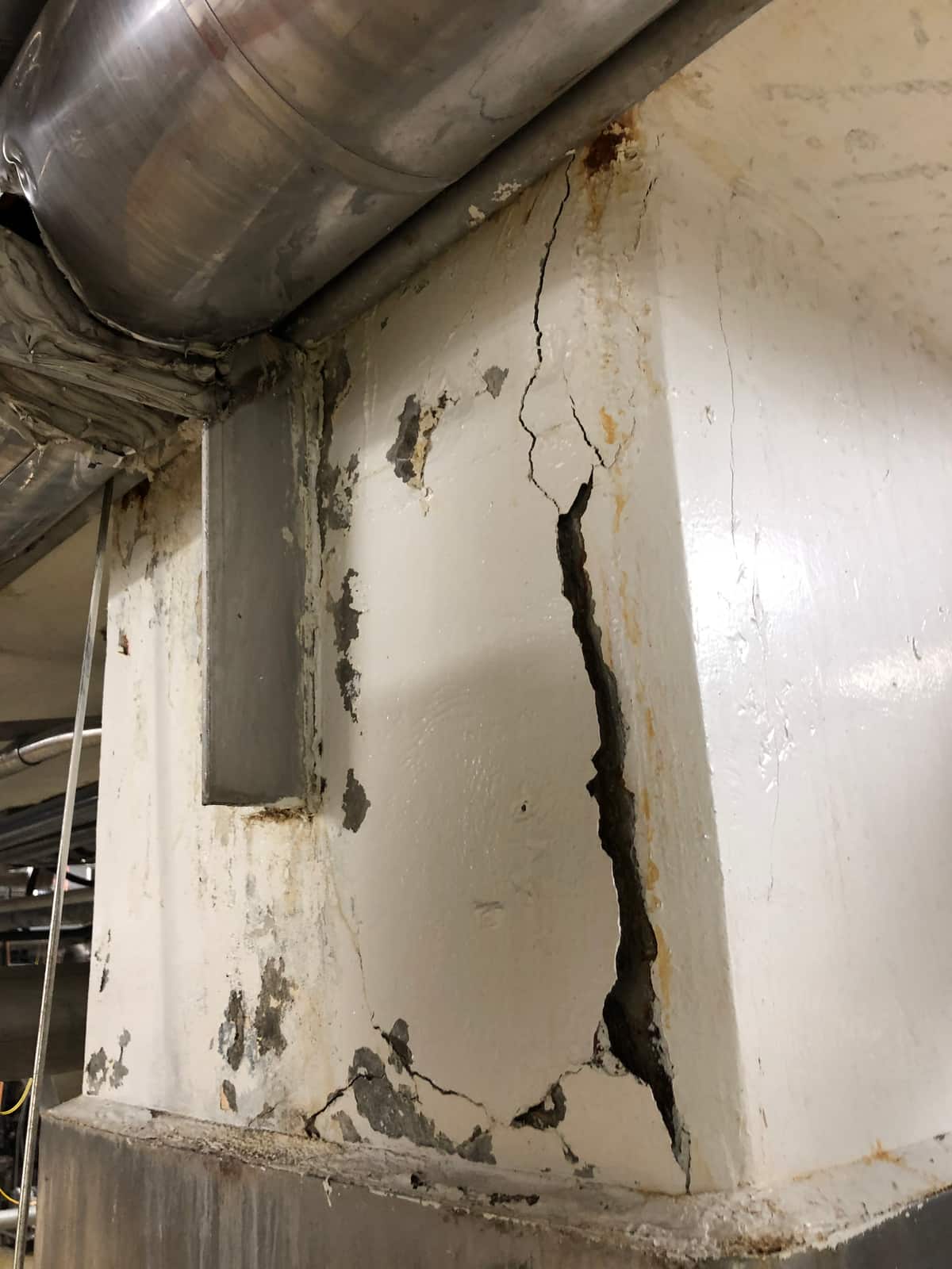 Painted concrete column with a wide open vertical crack and spalling.