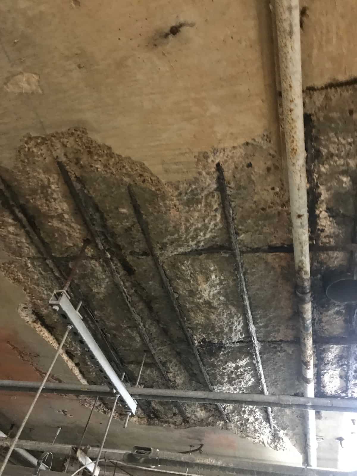 Concrete wall with a large spalled area exposing corroded rebar in a food plant.