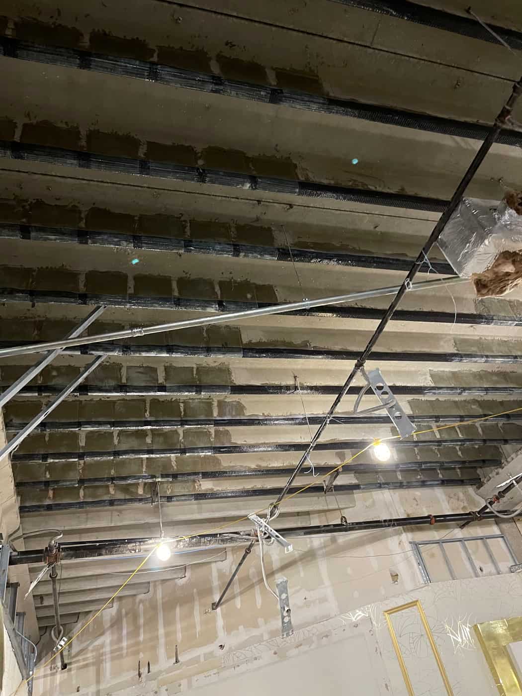 Concrete joists with black carbon fiber wraps at their ends along a girder.