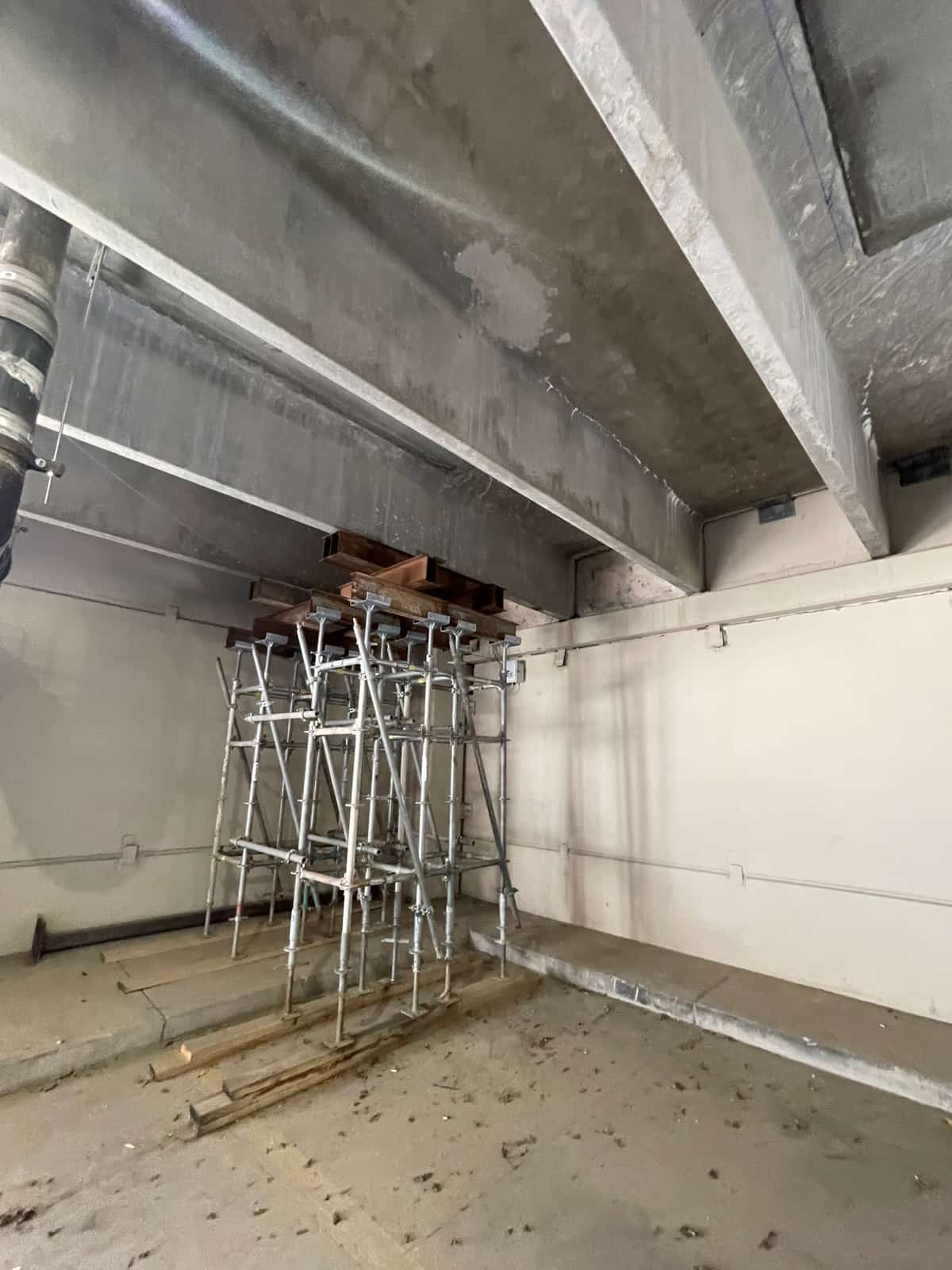 Shoring tower under concrete beams against a wall in a concrete room.