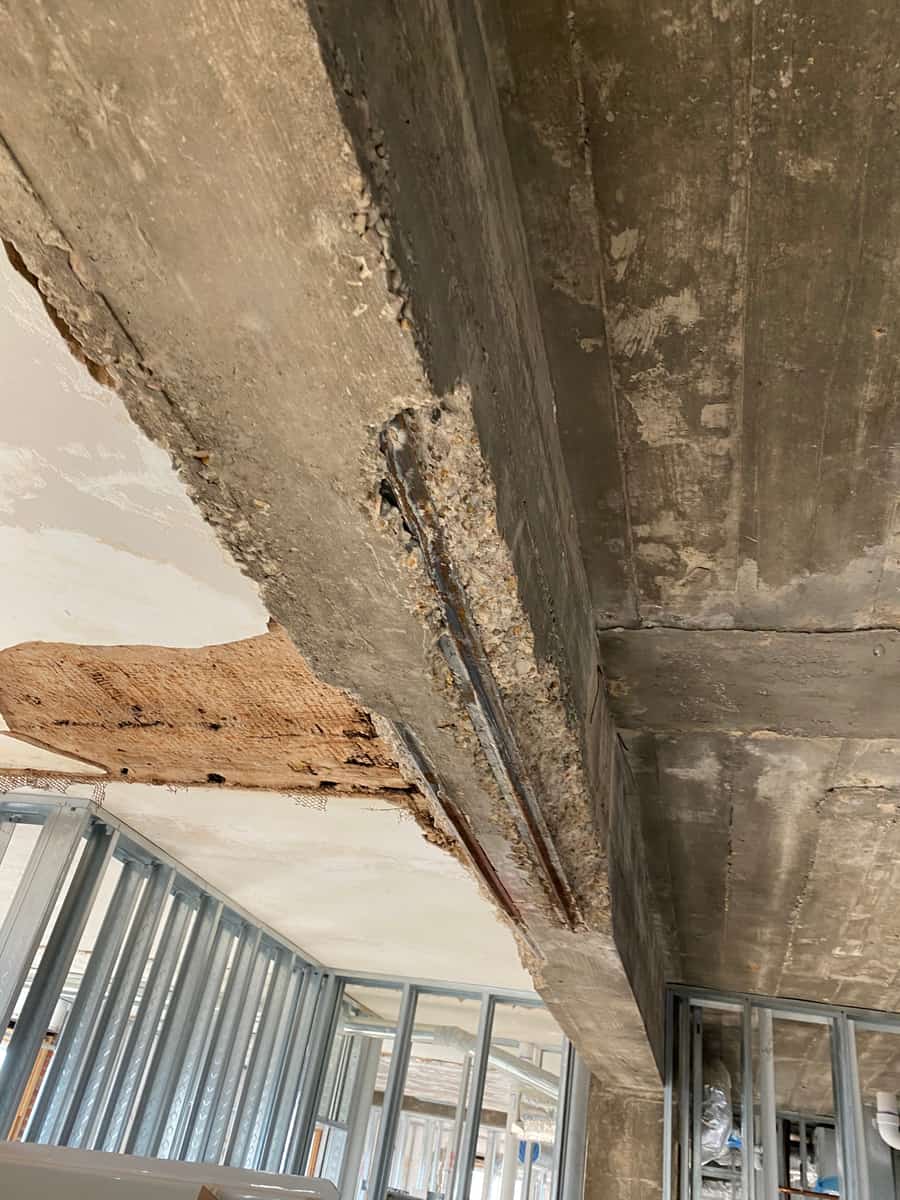 Beam soffit with a long spall and exposed bar above metal stud walls.