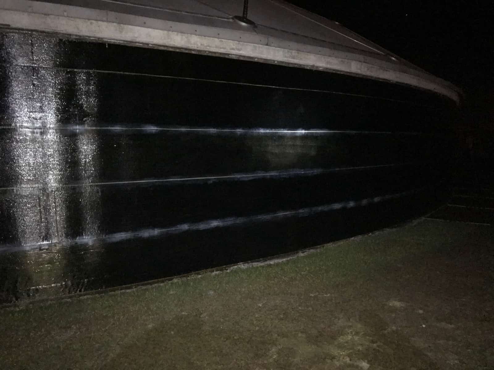 Curved tank wall wrapped in horizontal bands of black carbon fiber at night.