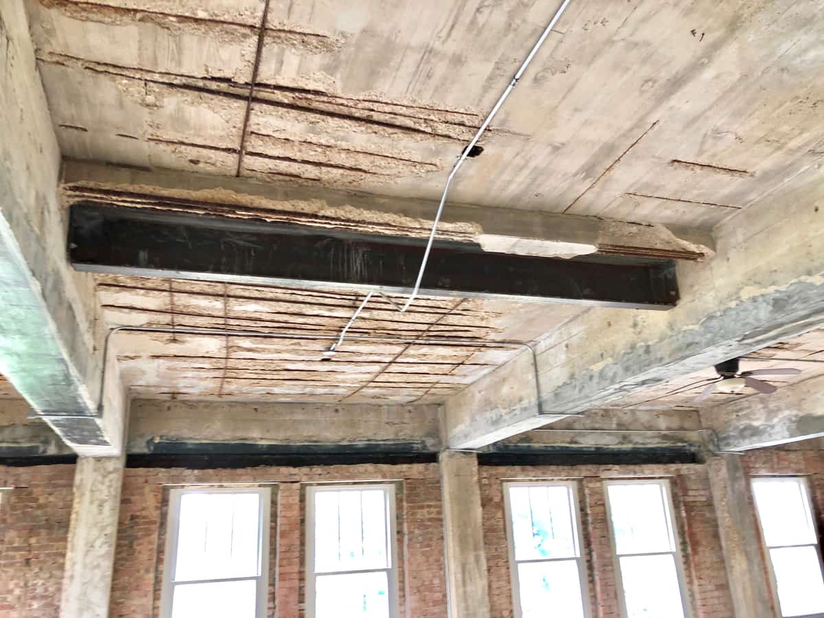 Slab soffit with spalled cover exposing rebar above a beam with carbon fiber on its soffit.