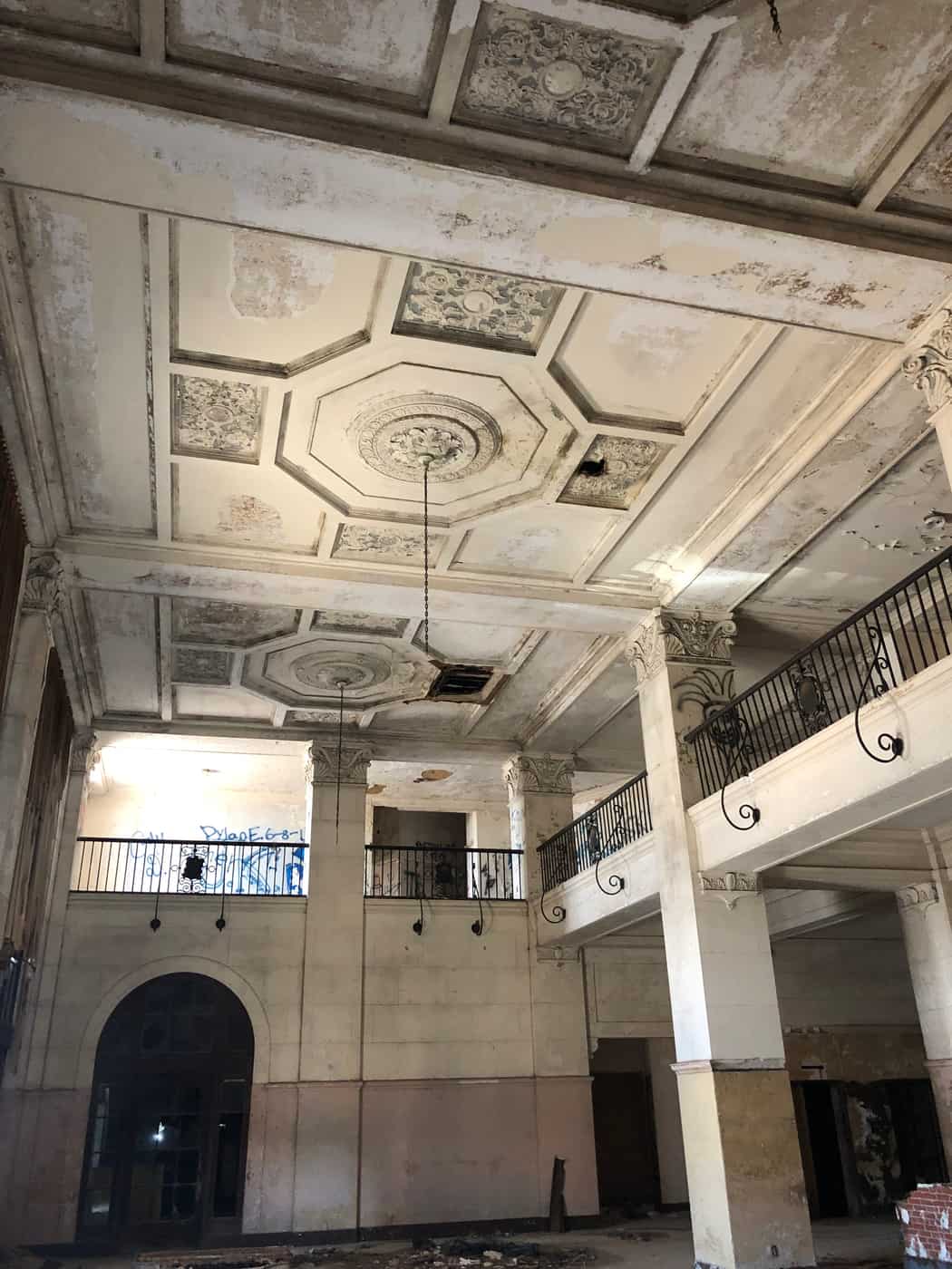 Two-story historic hotel lobby with a coffered ceiling, columns and balconies before renovation.