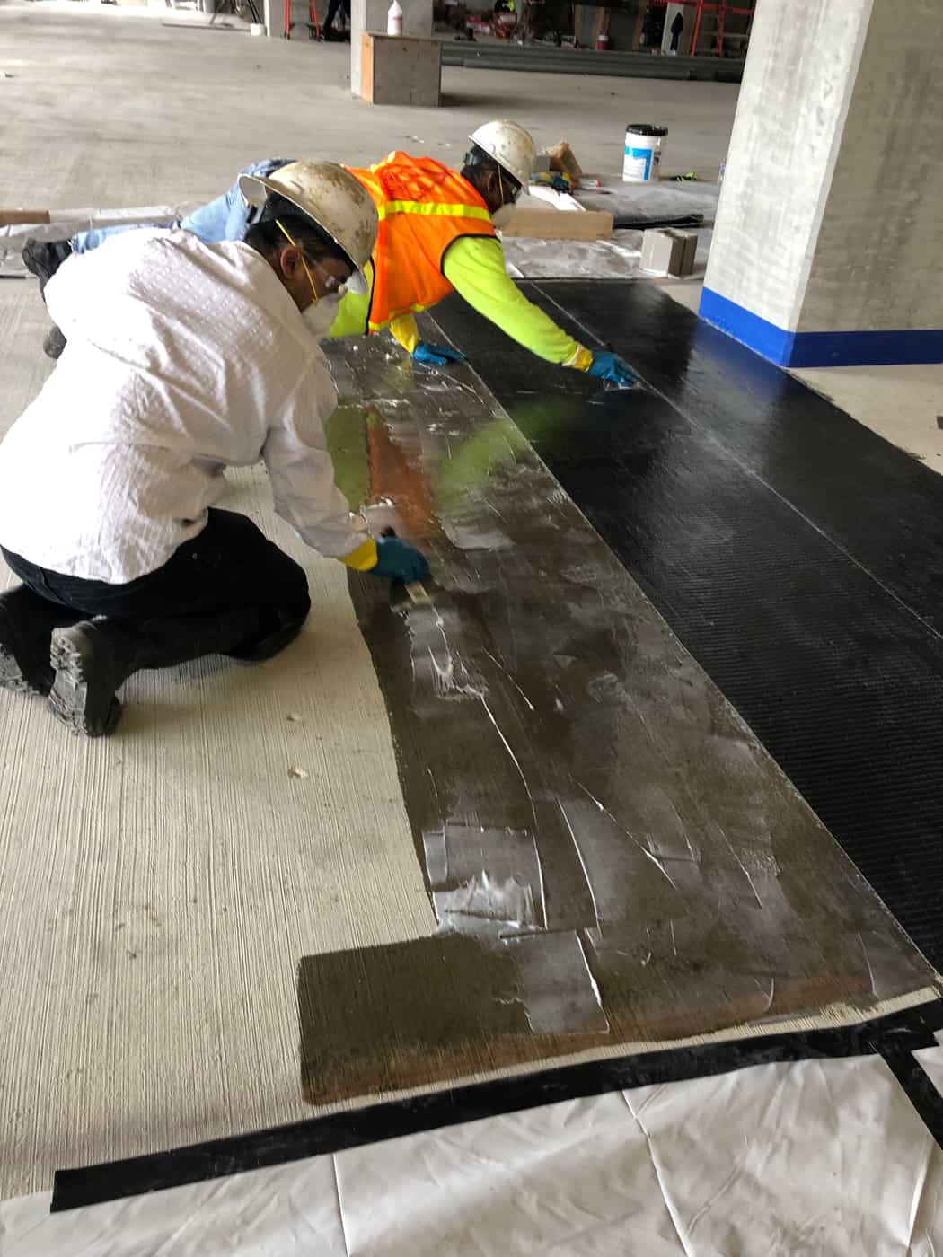 Two workers applying epoxy and carbon fiber sheet on a concrete deck.
