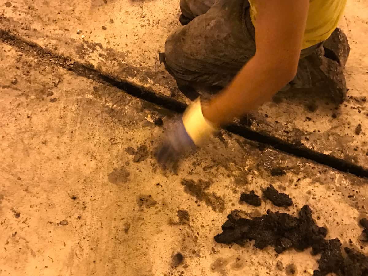 Gloved worker cleaning old sealant out of a joint in a concrete floor.