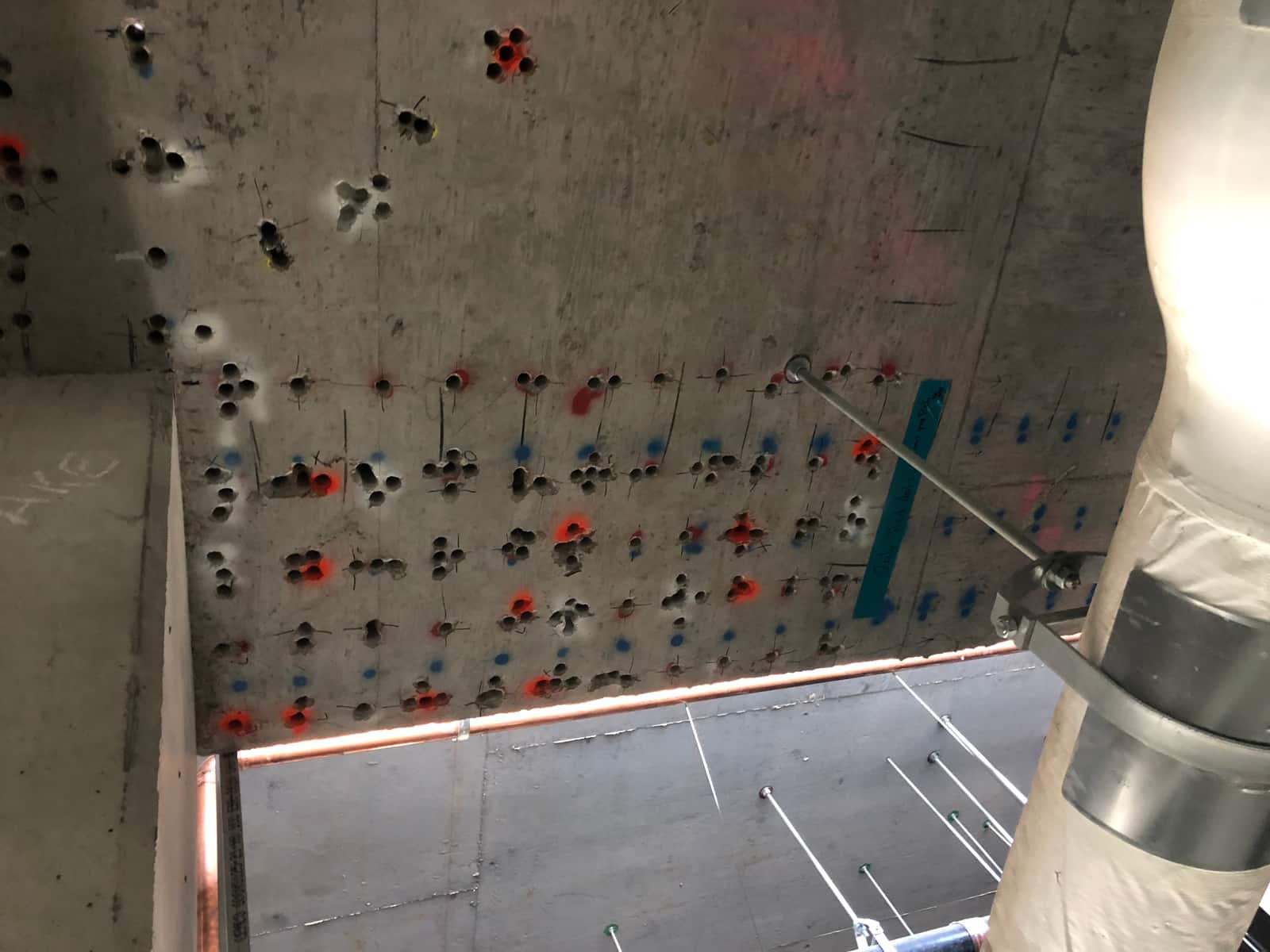 Grid of drilled holes with red and blue layout marks in a slab soffit at a column.