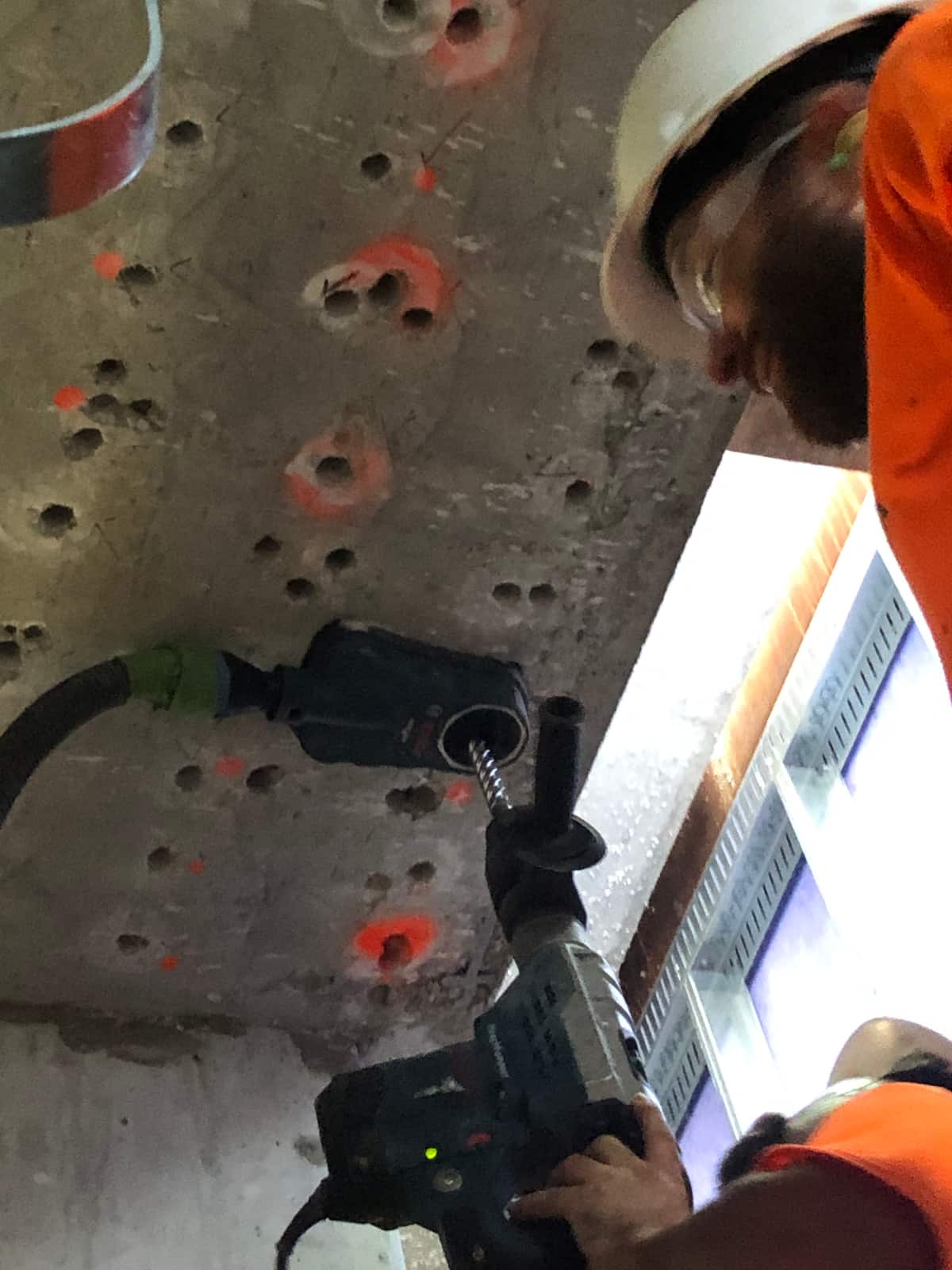 Worker drilling upward into a slab soffit with a dust-extracting hammer drill.