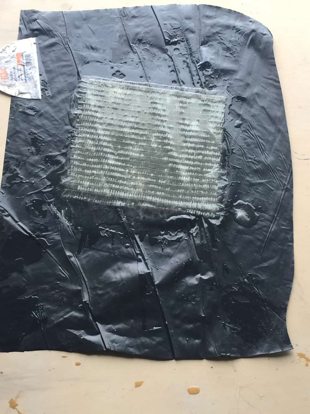 Test patch of saturated glass fiber fabric on a black membrane sheet.
