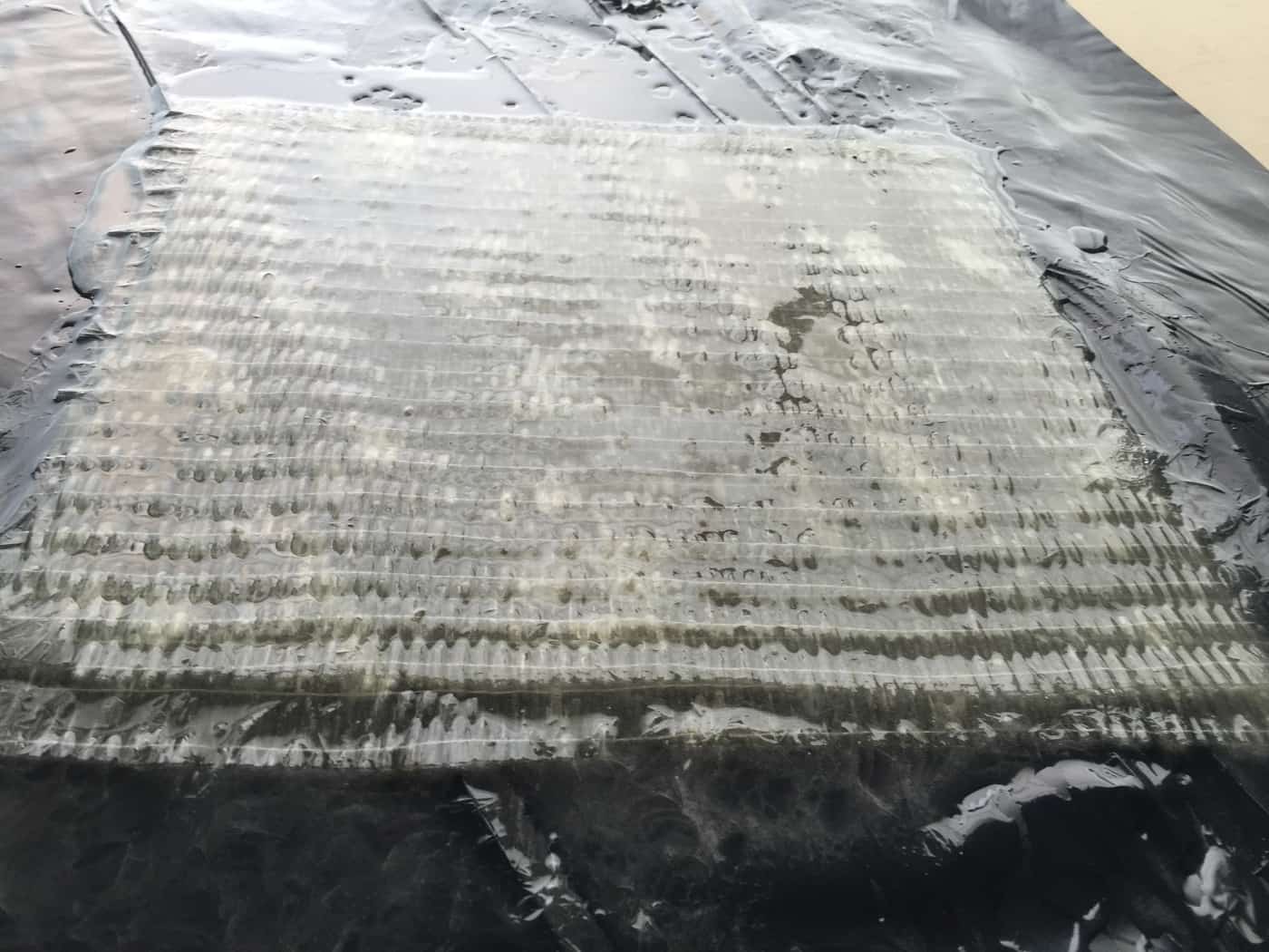 Close-up of a saturated glass fiber fabric test patch on a dark membrane.