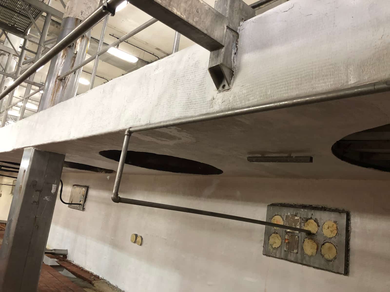 White-coated concrete support wall with tank outlet openings and a patched steel plate.