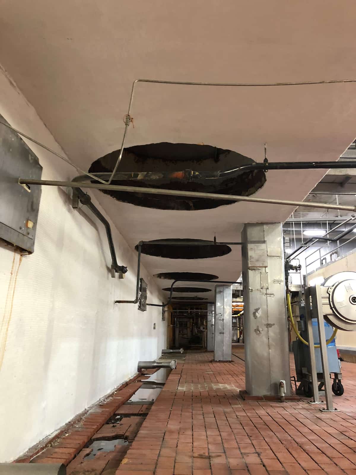 Long cellar aisle with white-coated concrete support walls under overhead tanks.