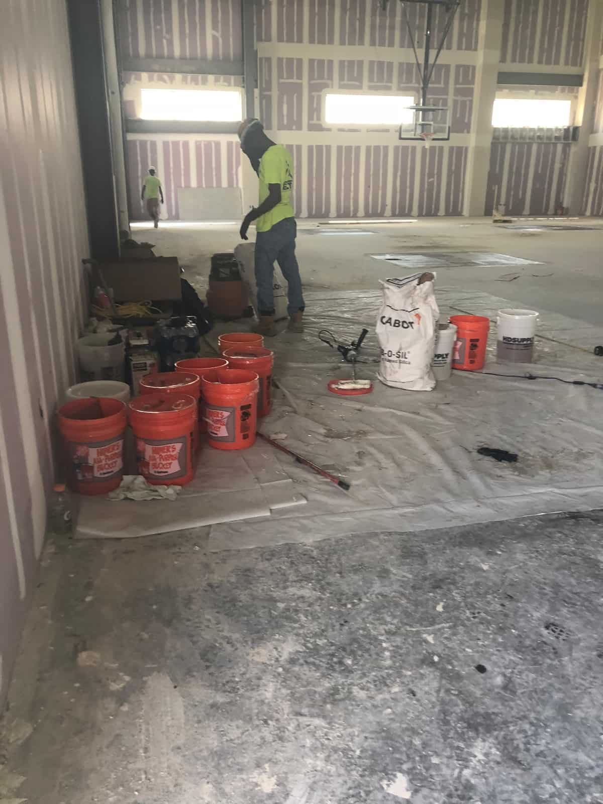 Worker mixing repair materials beside buckets and bags inside a metal building.