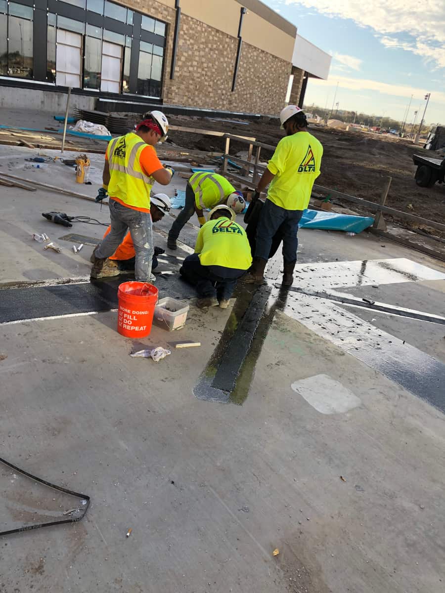 Workers kneeling to apply FRP strips on a concrete slab top.