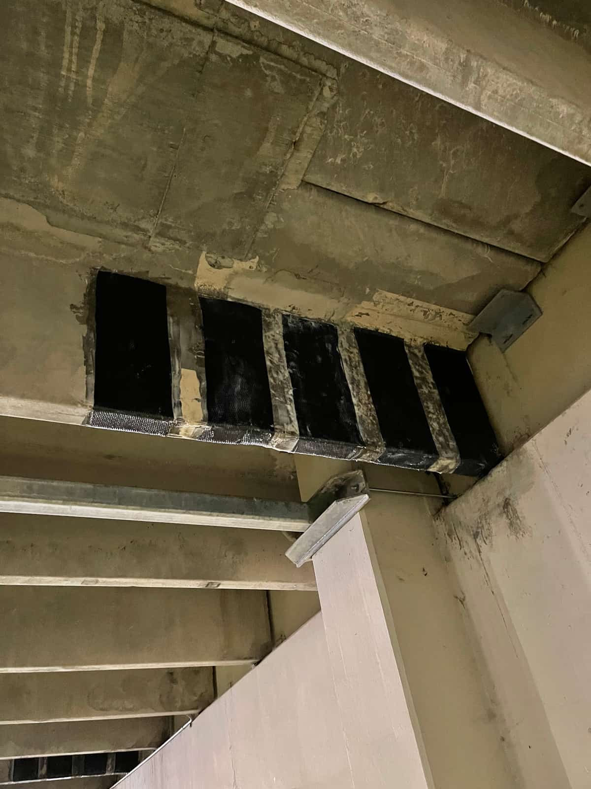 Black carbon fiber strips on the underside of a stepped stadium seating slab.