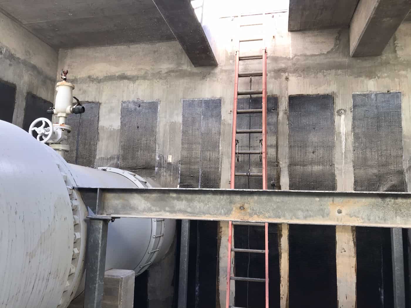 Rows of carbon fiber panels on concrete vault walls around a large pipe.