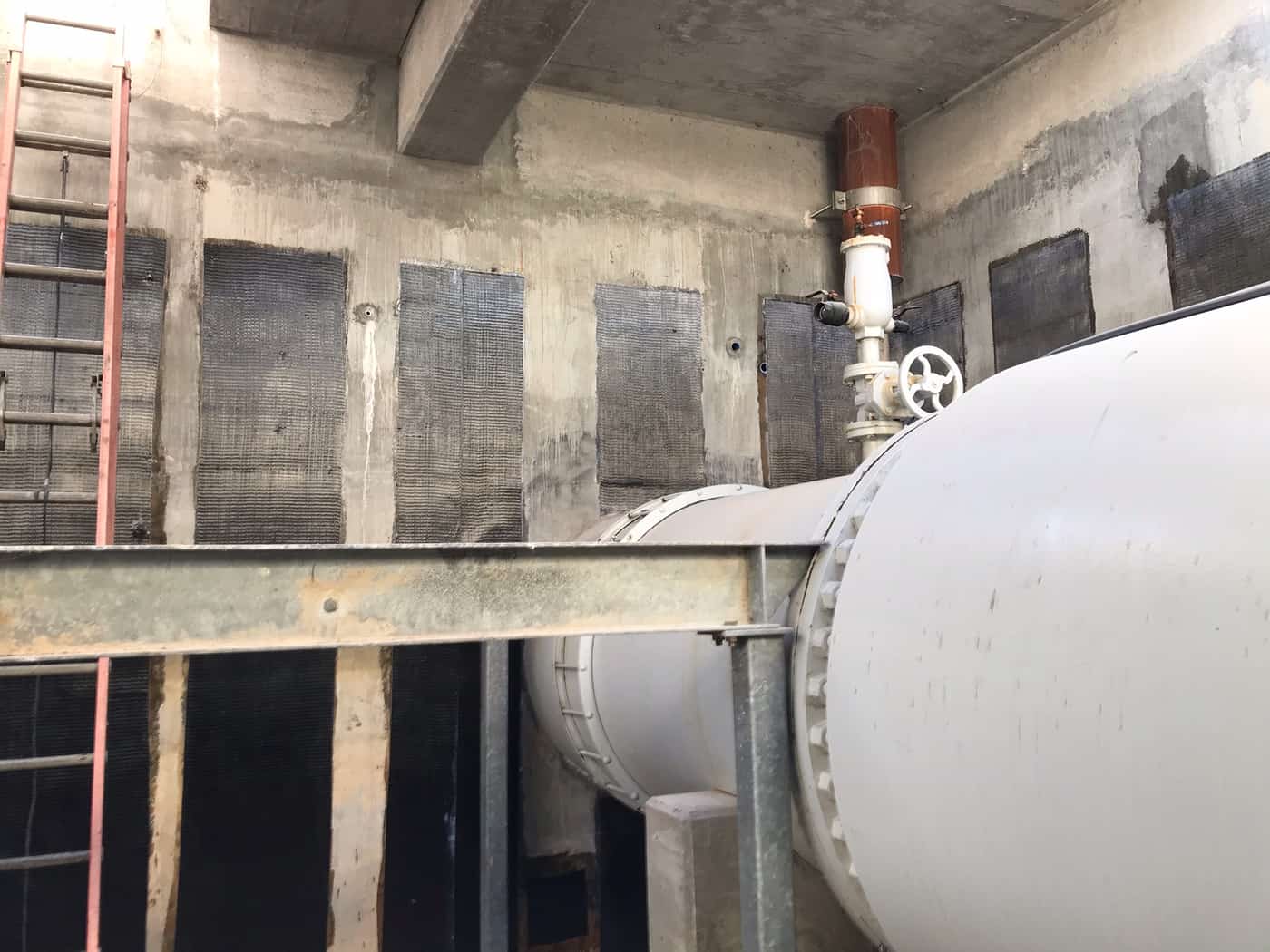 Vault walls with rows of carbon fiber panels around a steel beam, large pipe and ladder.
