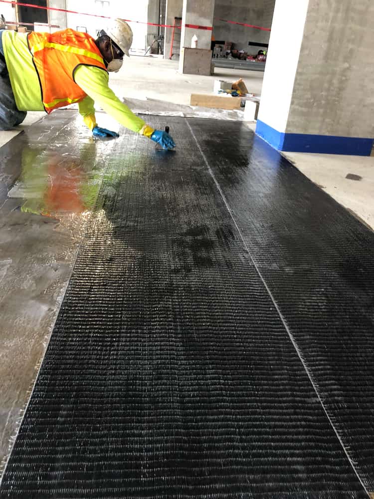 Worker pressing a carbon fiber sheet onto a concrete deck.