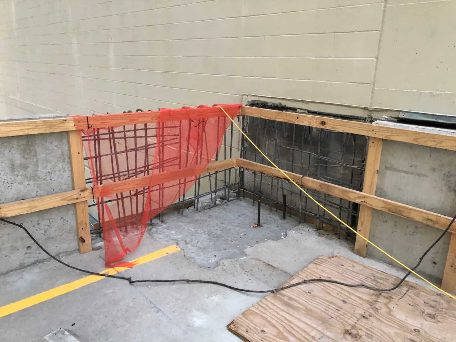 Timber formwork and rebar at a wall repair with orange safety netting.