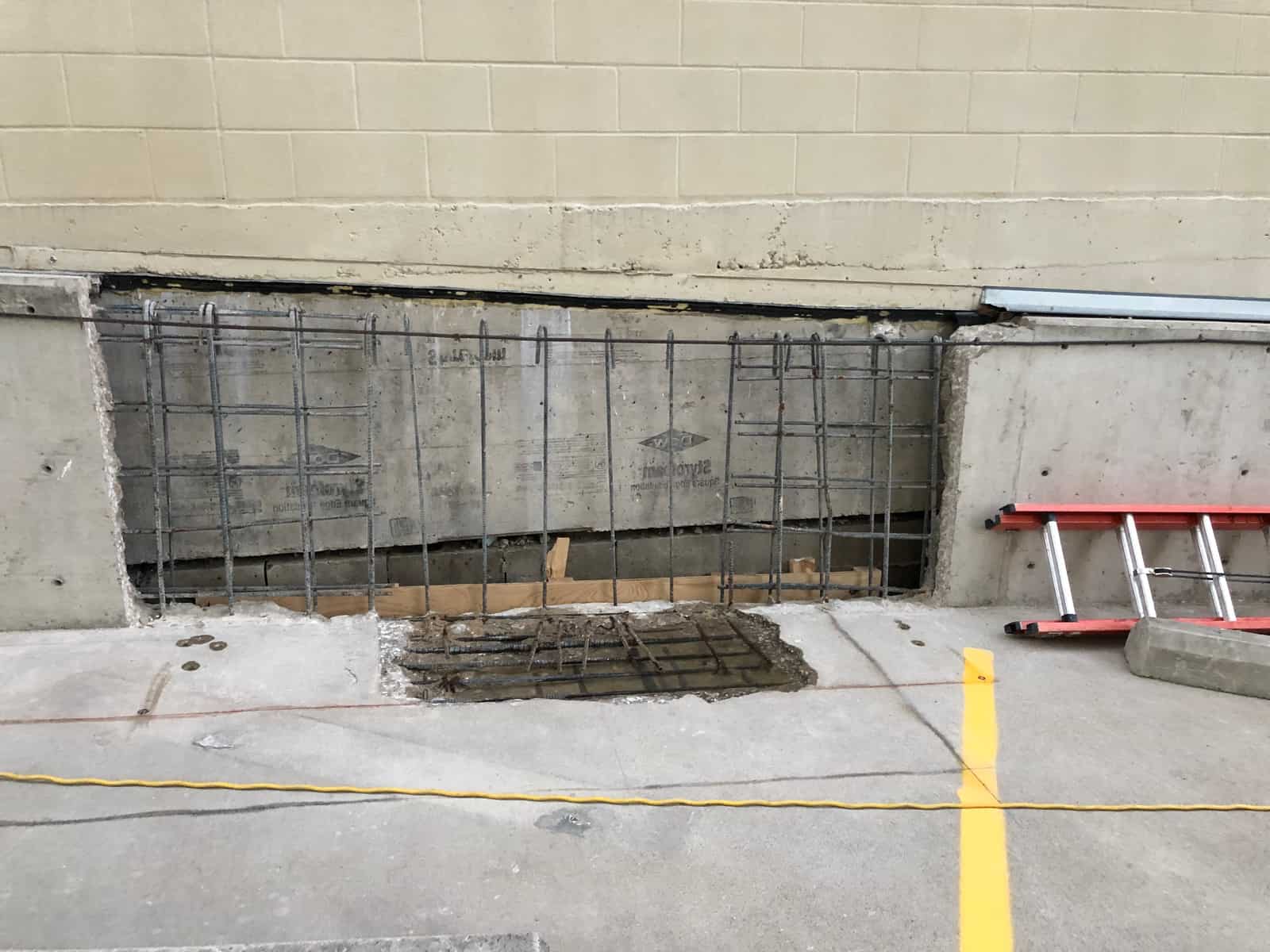 Removed concrete wall section with an exposed rebar mat and a ladder.