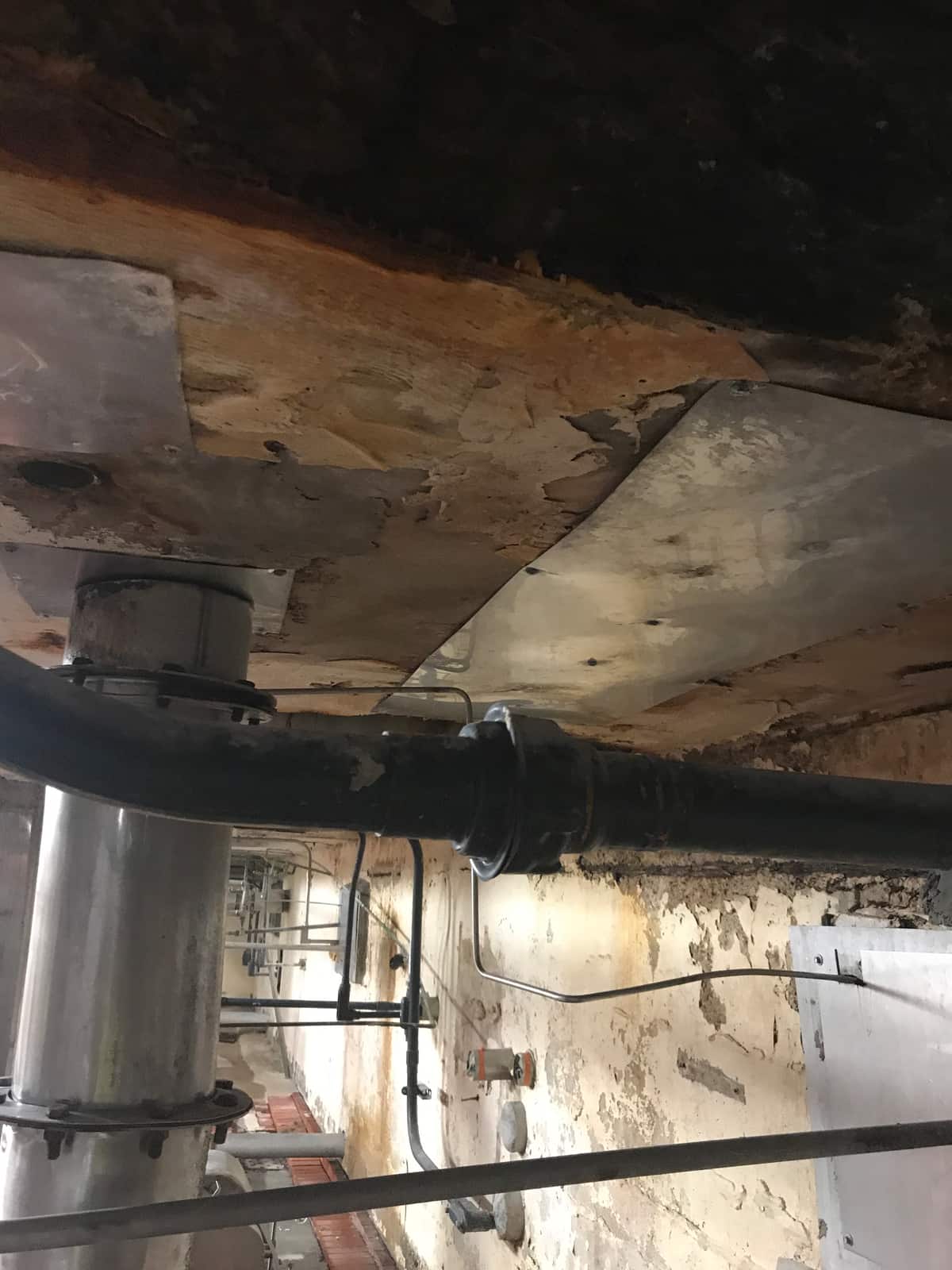 Deteriorated concrete beam soffit with a steel plate and pipe below.