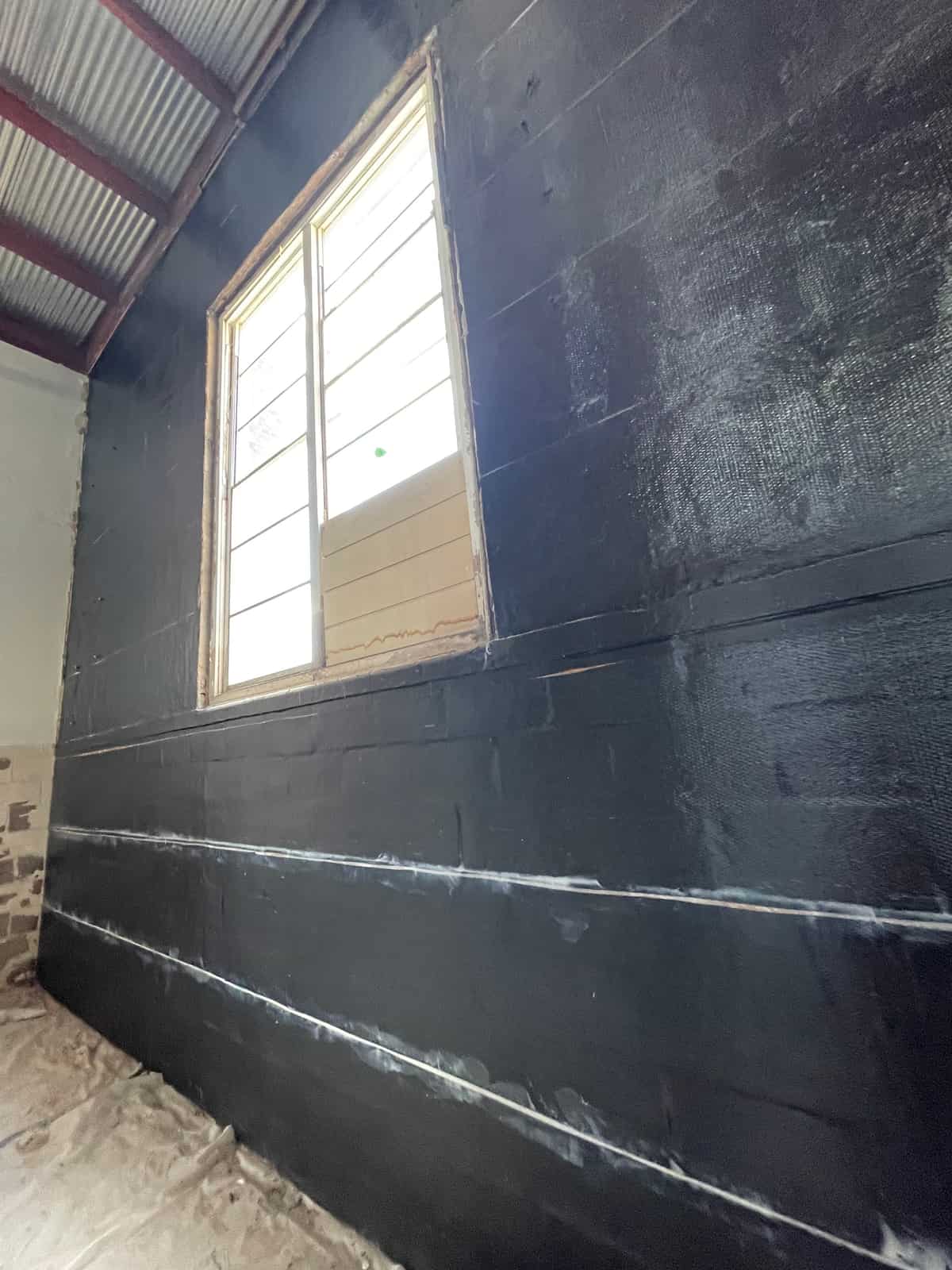 Black carbon fiber fabric covering a masonry wall around a window.