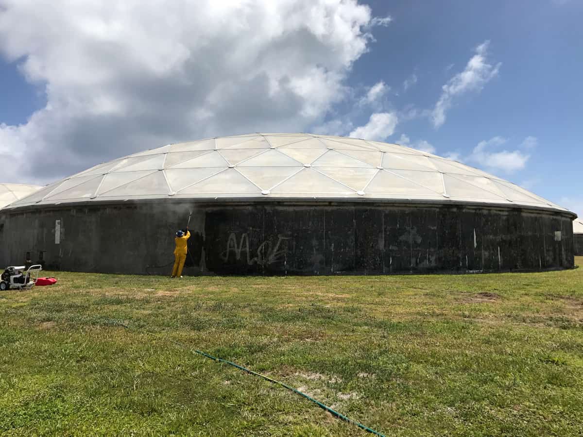 Circular concrete tank with an aluminum dome while a worker prepares the lower wall.