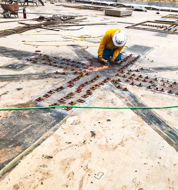 Worker at the center of a star pattern of FRP strips and anchor plates on a slab top.