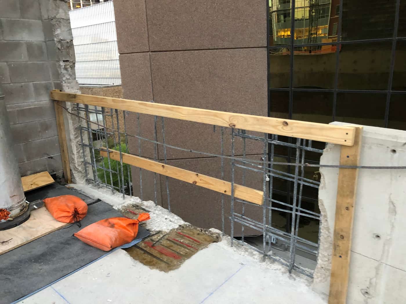 Cut parapet with exposed rebar, a timber rail and sandbags.