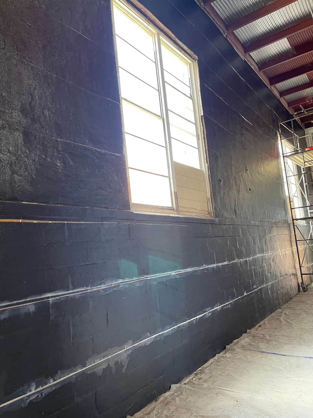 Full-height black carbon fiber fabric with lap seams on a masonry wall around a window.