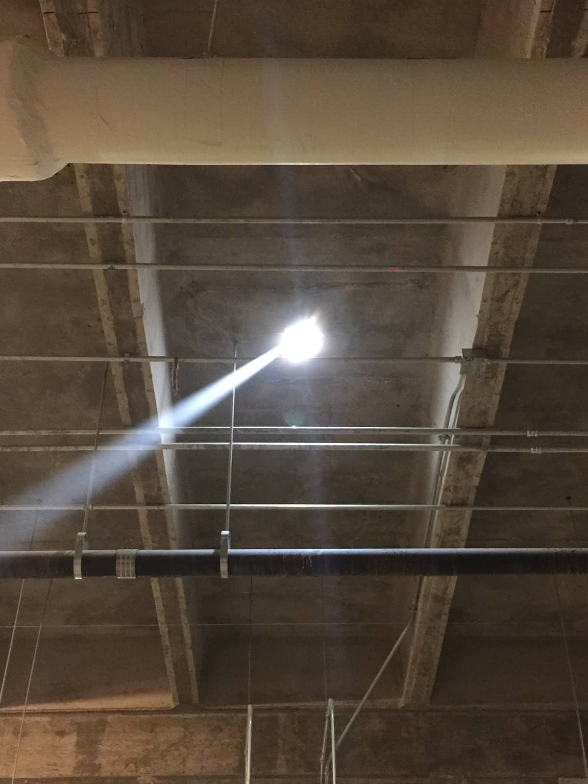 Underside of concrete stadium seating with sloped raker beams, conduit and a light.