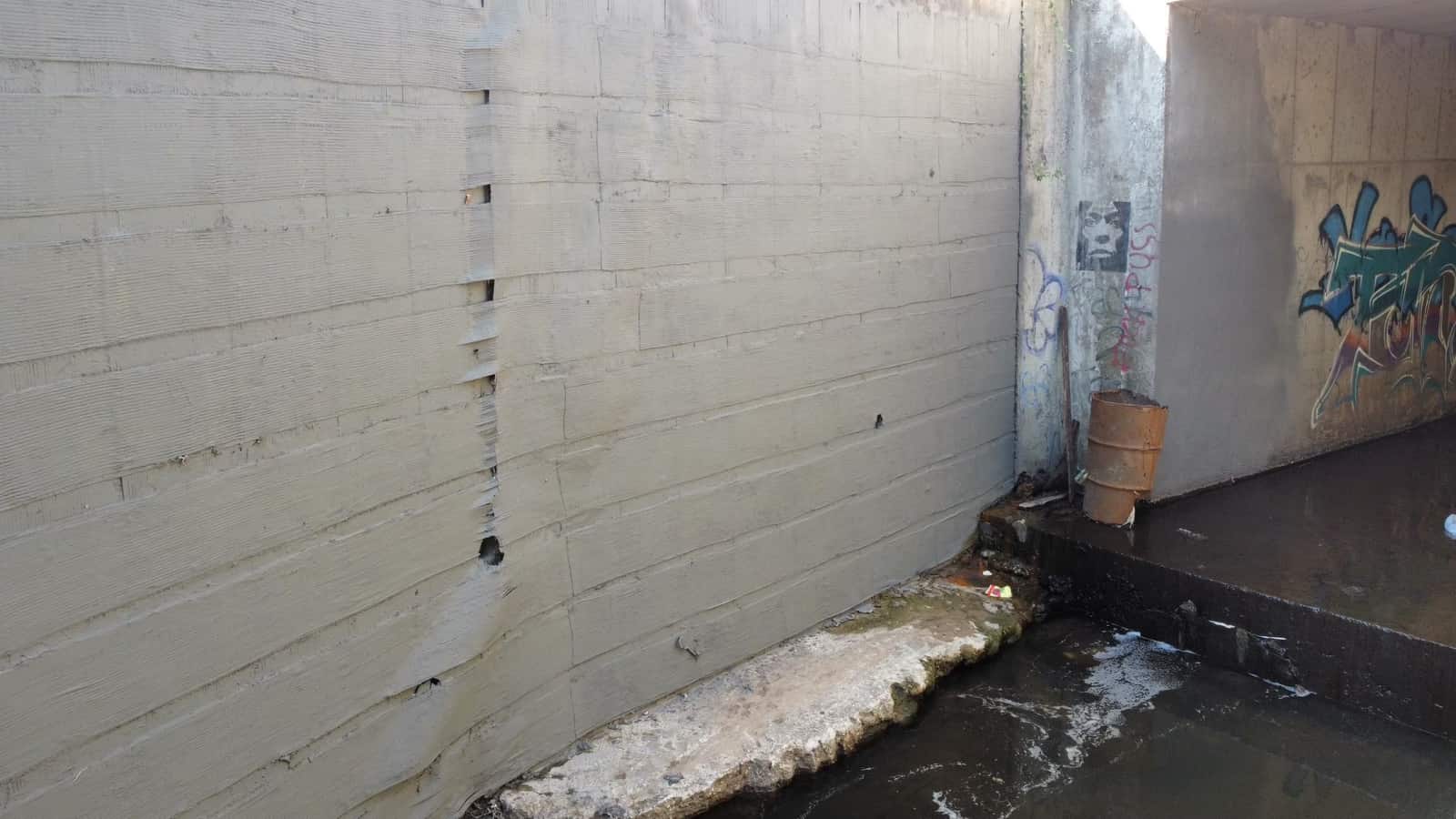 Concrete channel wall with cracks beside a culvert opening.