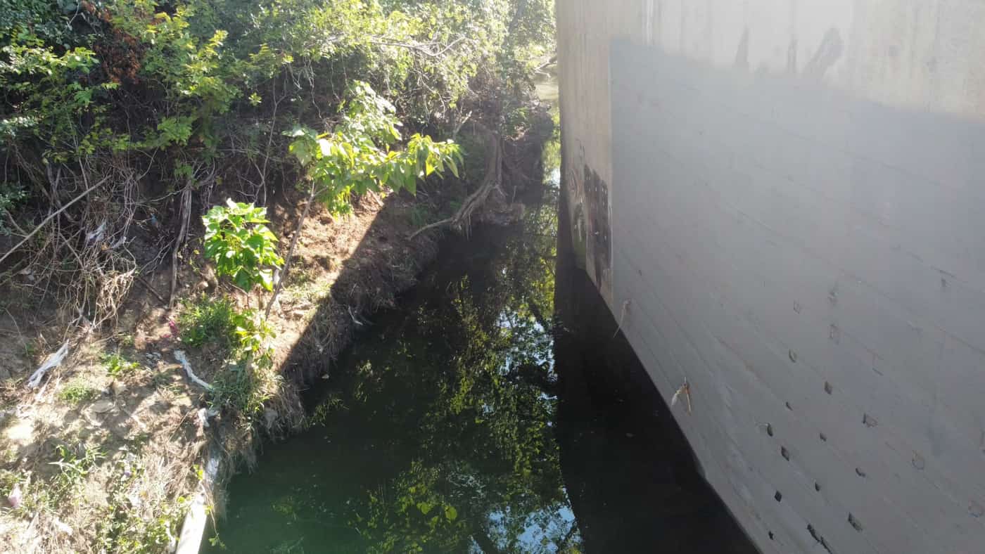 Board-formed concrete channel wall over water beneath a roadway.
