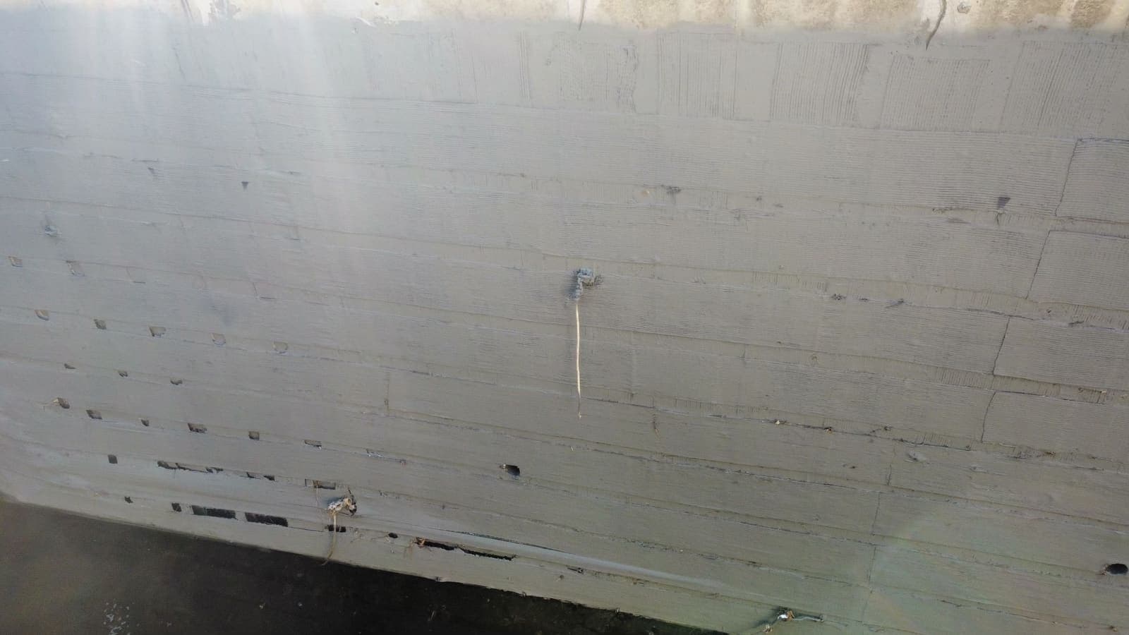 Concrete wall face with form-tie holes and damage near the waterline.