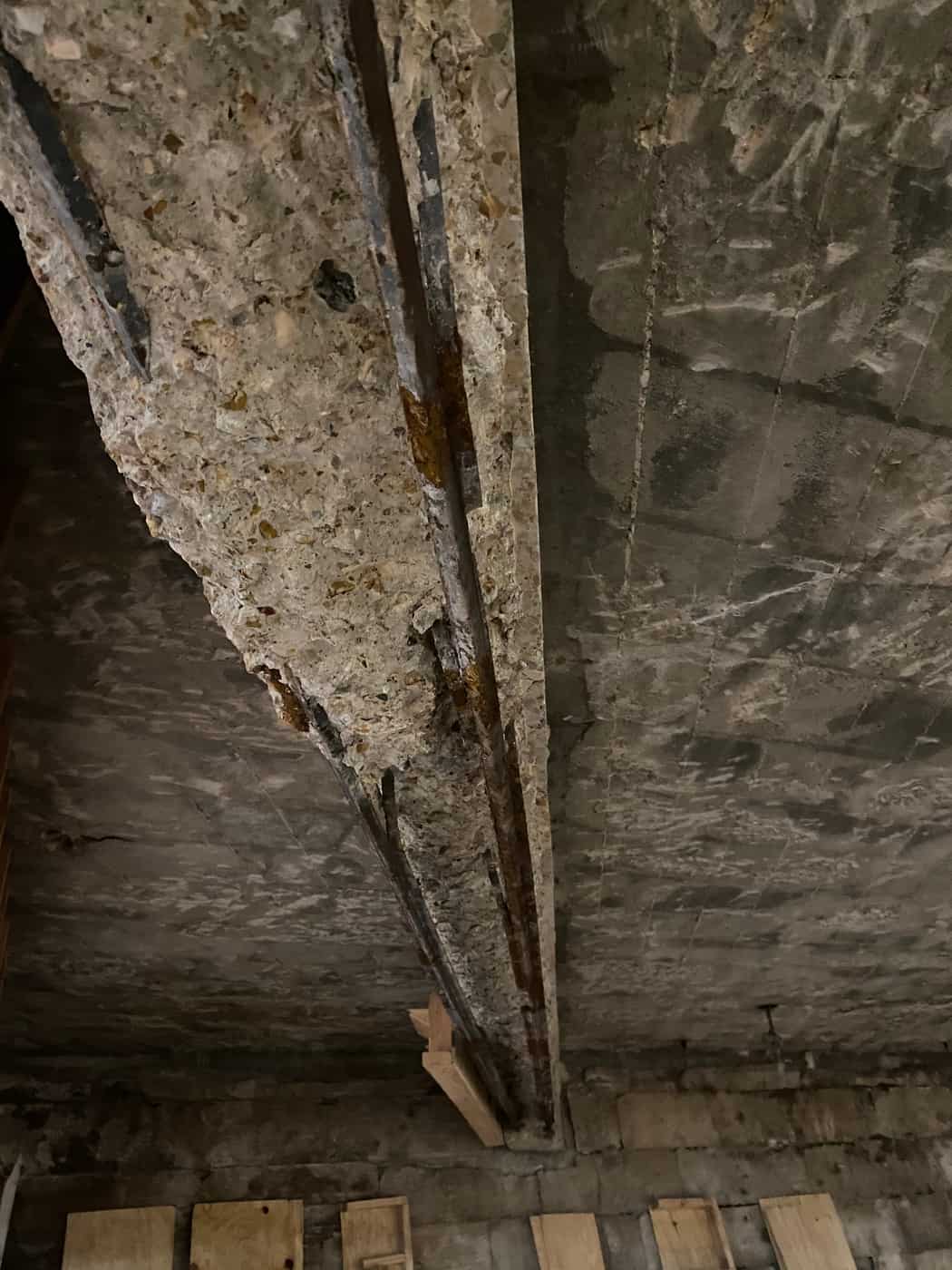 Concrete beam with spalled cover and exposed reinforcing bars in a basement.