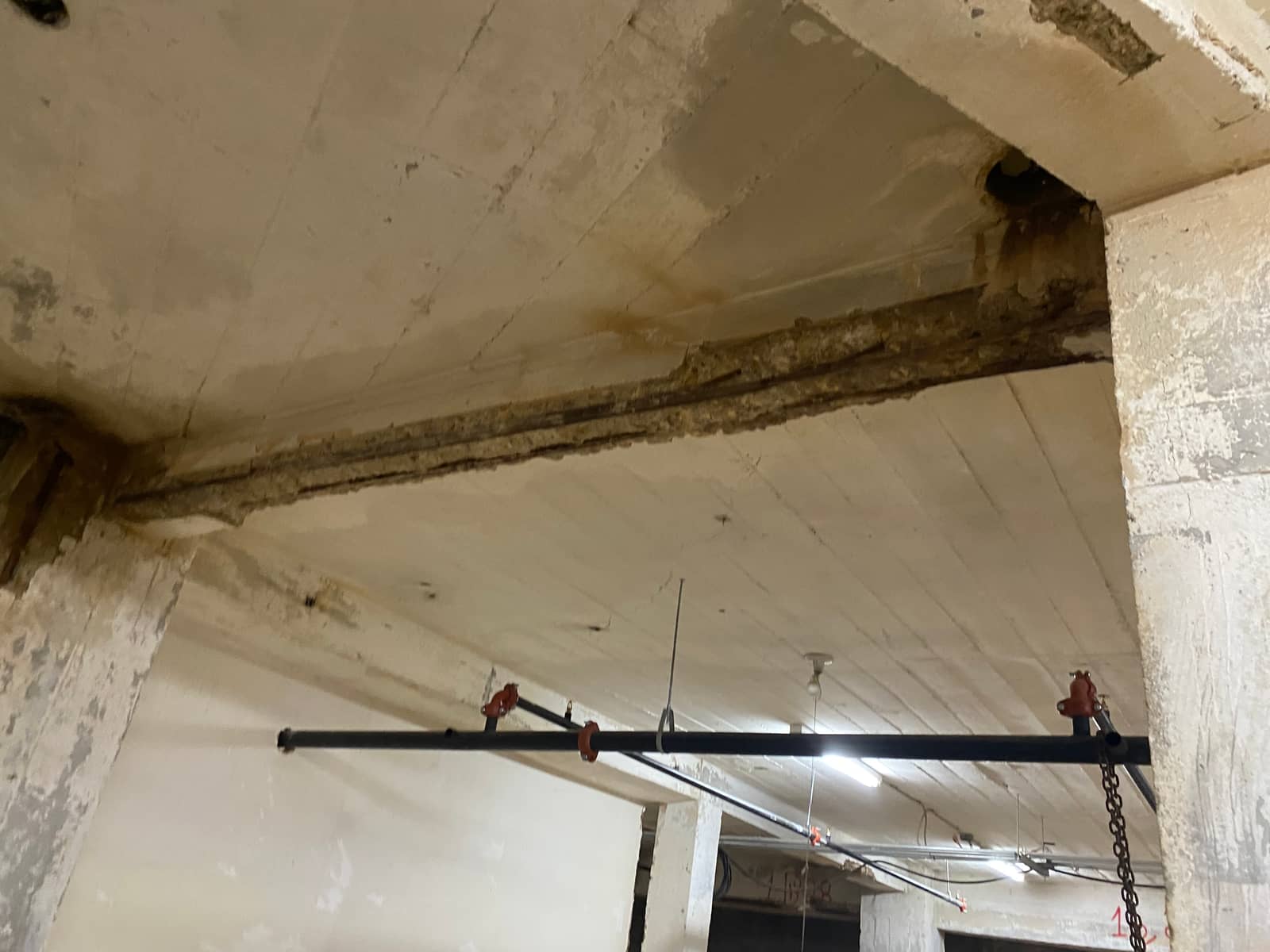 Concrete beam with a spalled soffit and exposed rebar spanning between columns.