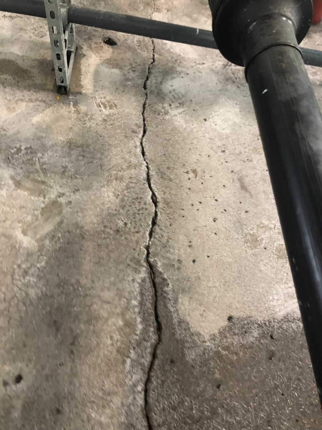 Long crack running through a concrete floor slab beside a pipe and strut.