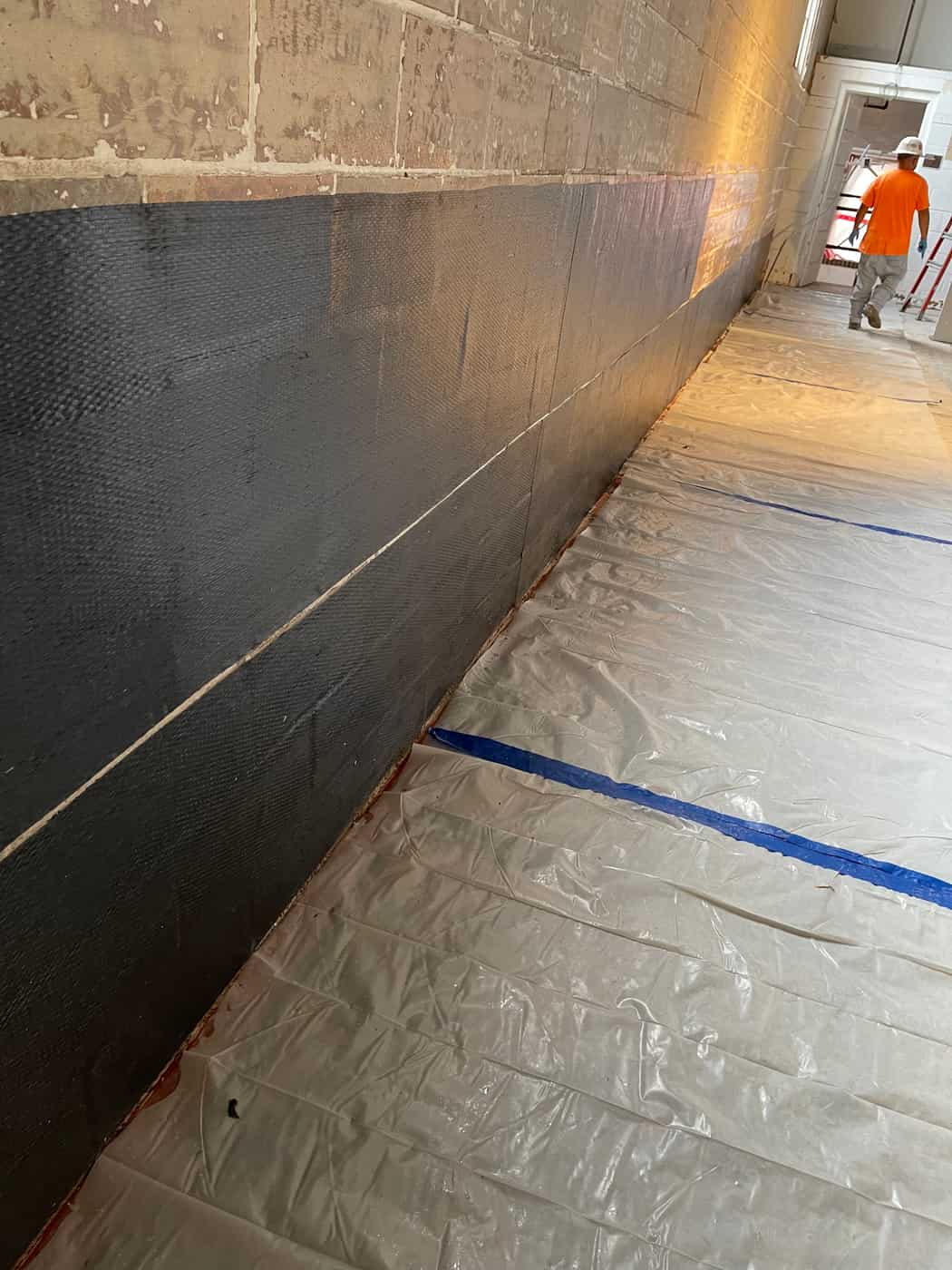 Black carbon fiber fabric on a lower masonry wall along a hallway.