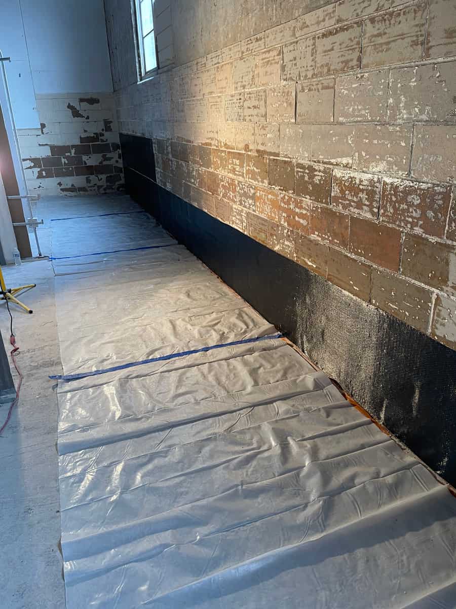 Lower band of black carbon fiber fabric on a masonry wall over plastic floor protection.