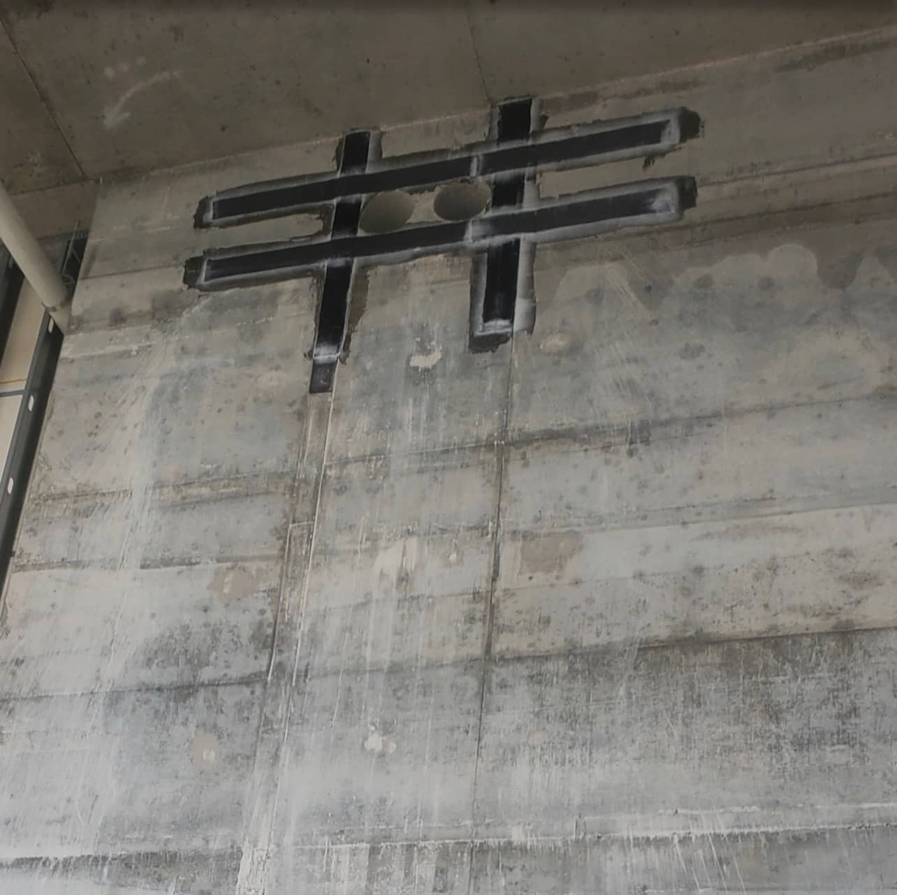 Concrete wall with hash-shaped black composite strips around a small penetration.