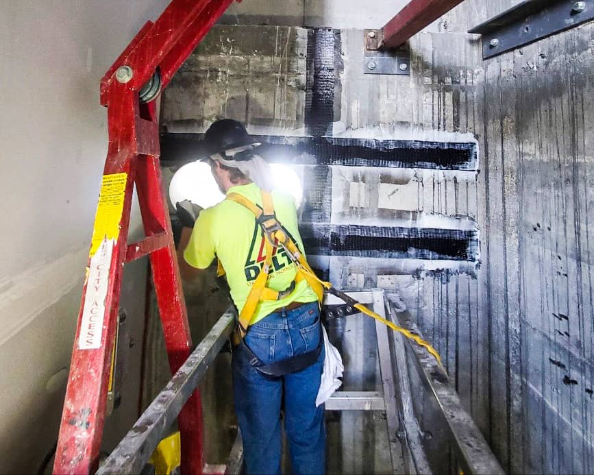 Installer placing black composite strips around a wall penetration in a shaft.