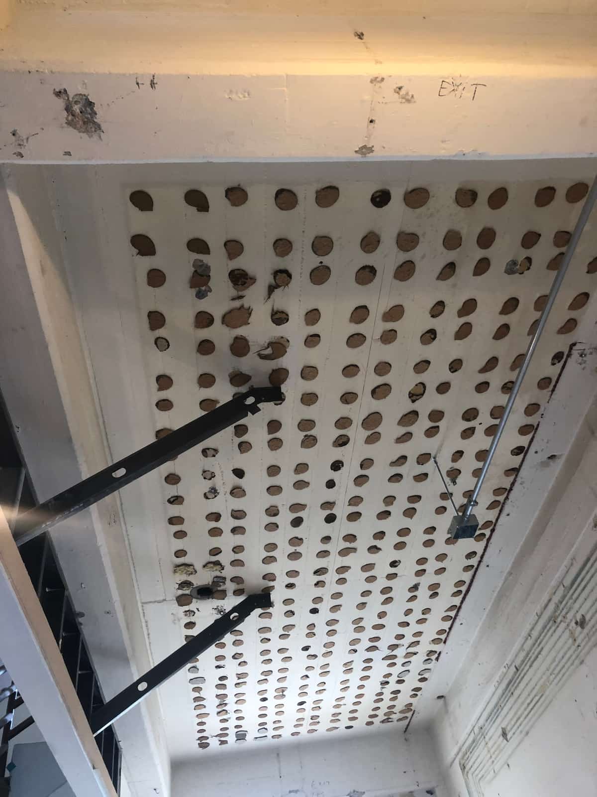 Soffit covered in a dense grid of drilled and filled holes with steel struts.